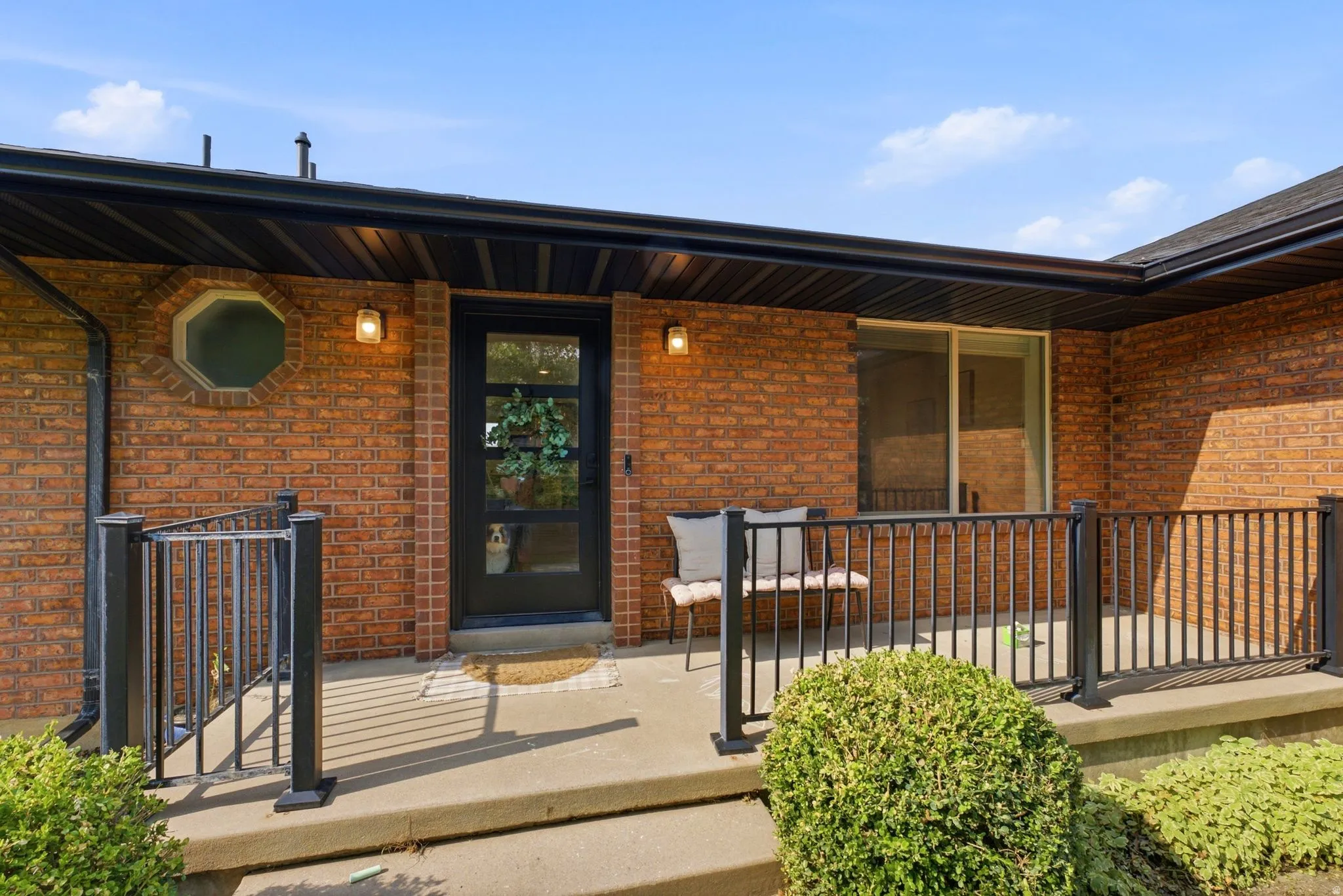 Brick exterior featuring a covered entry, black metal railing, and a modern black entry door with frosted glass