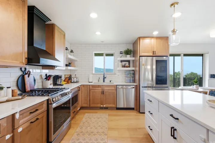 Gourmet kitchen featuring light wood cabinetry, white subway tile backsplash, stainless steel appliances, a center island with white countertop, and light wood-finish flooring