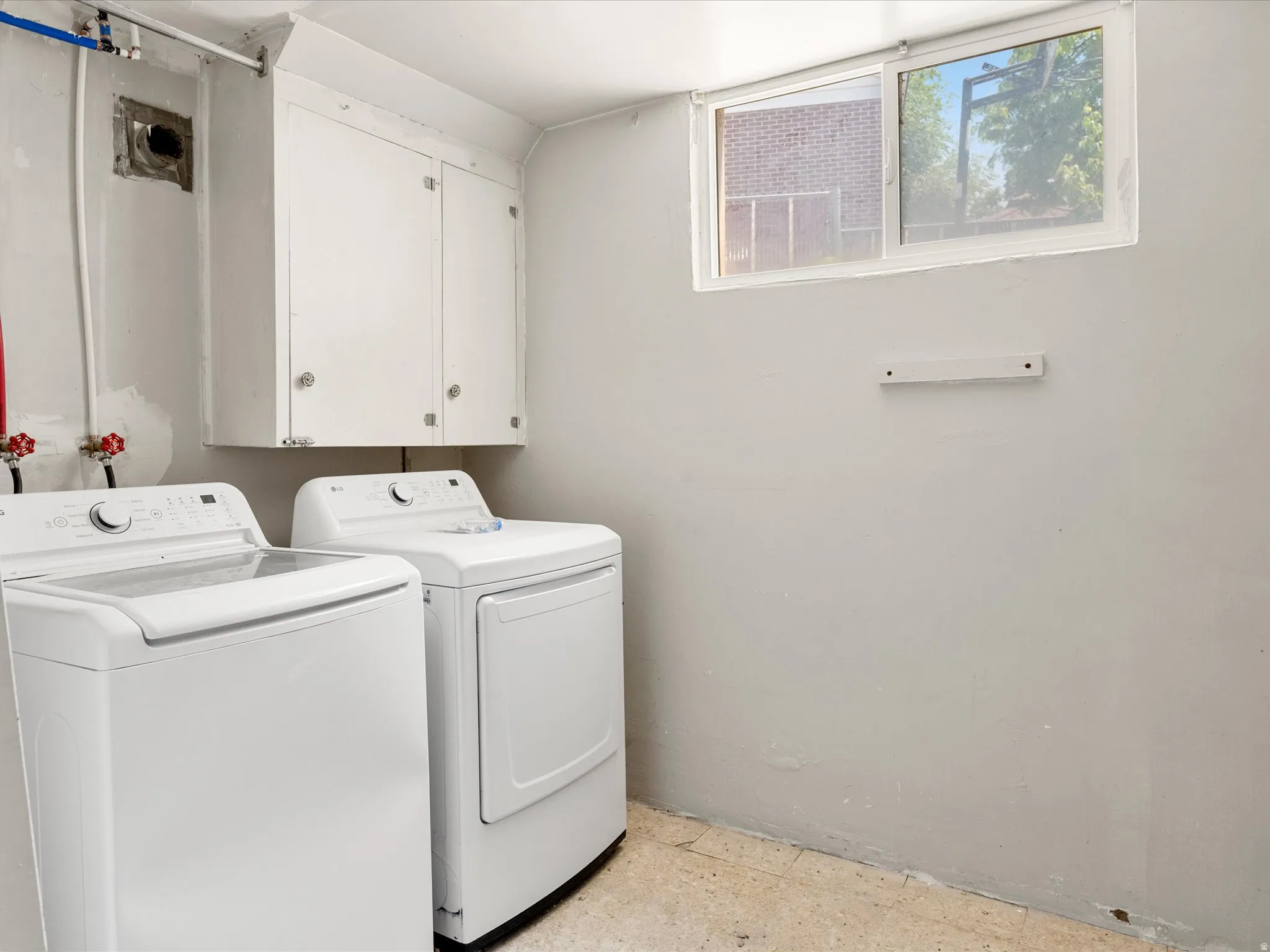 Laundry area featuring a sliding window, white upper cabinetry, and exposed plumbing