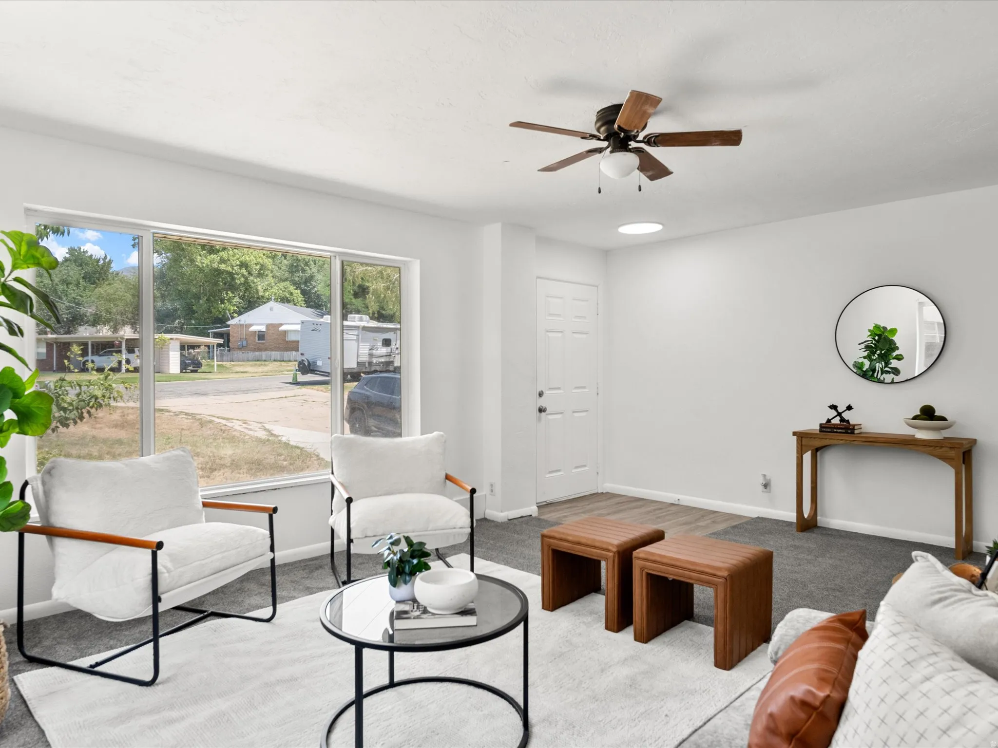 Living area featuring a large picture window, ceiling fan, and mixed flooring with carpet and wood-finish sections