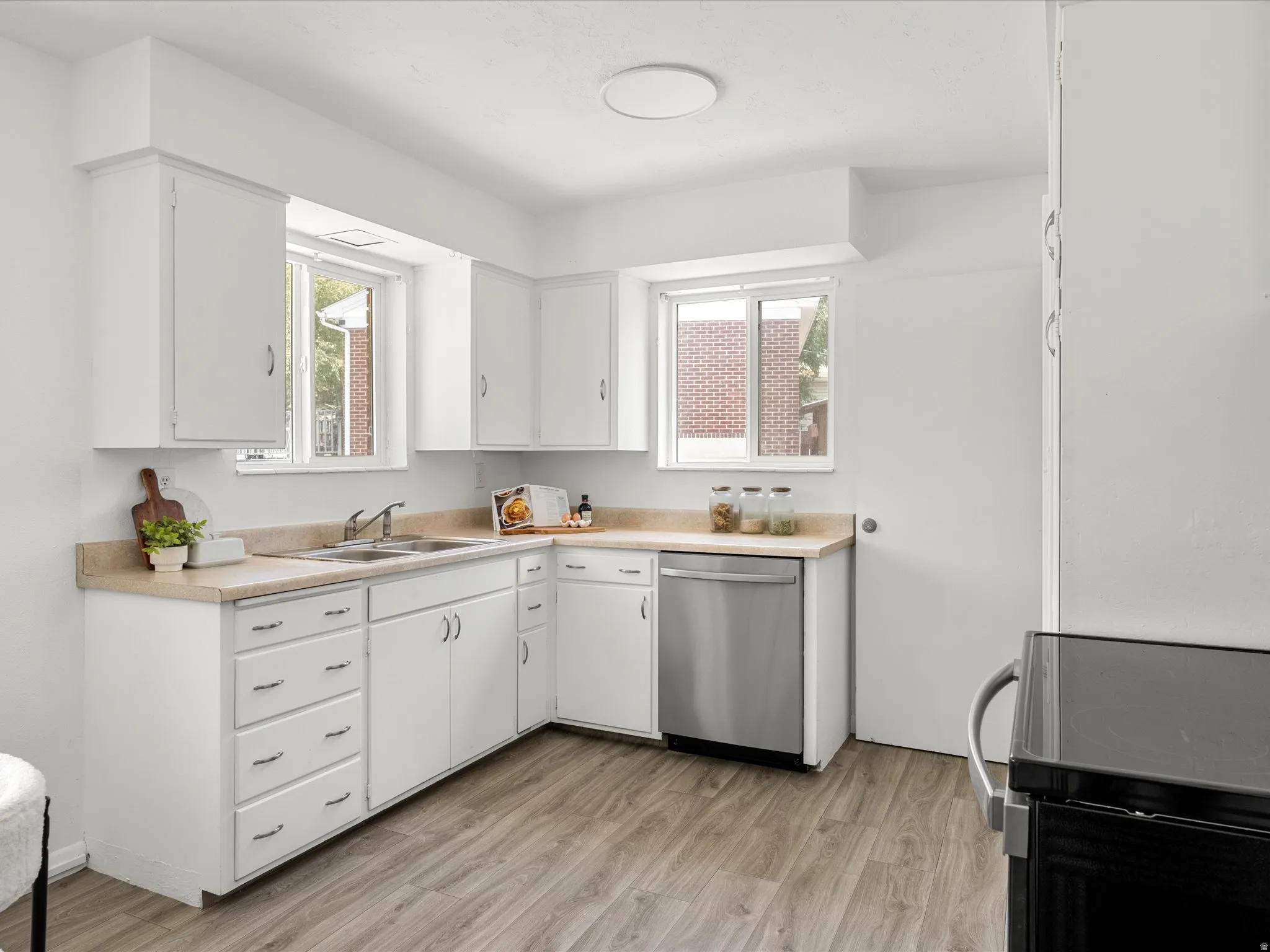 Kitchen featuring white cabinetry, light-toned countertops, a stainless steel dishwasher, and wood-finish flooring