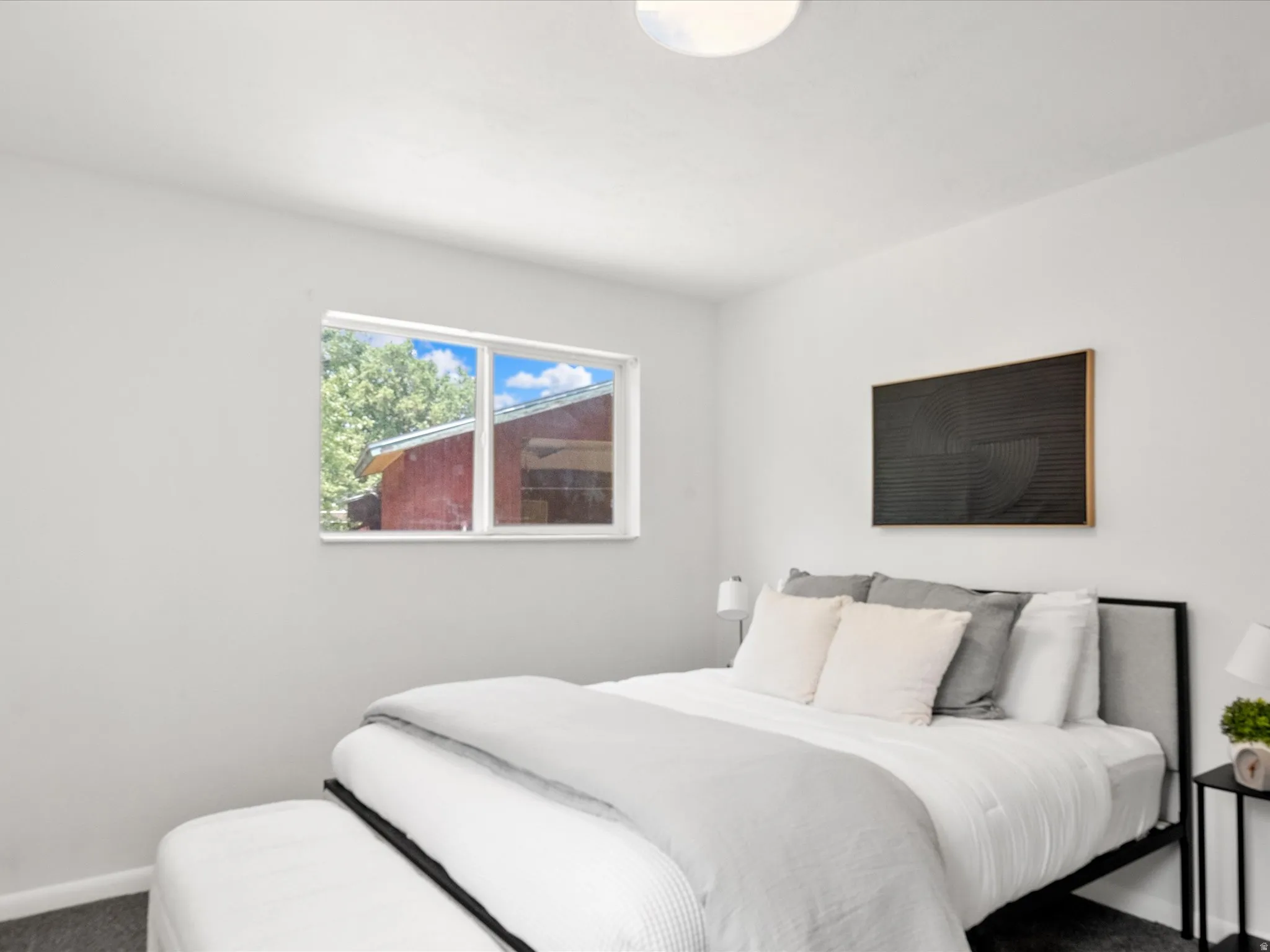Bright bedroom featuring a double-pane window, flush-mount ceiling light, light gray painted walls, and dark gray carpet flooring