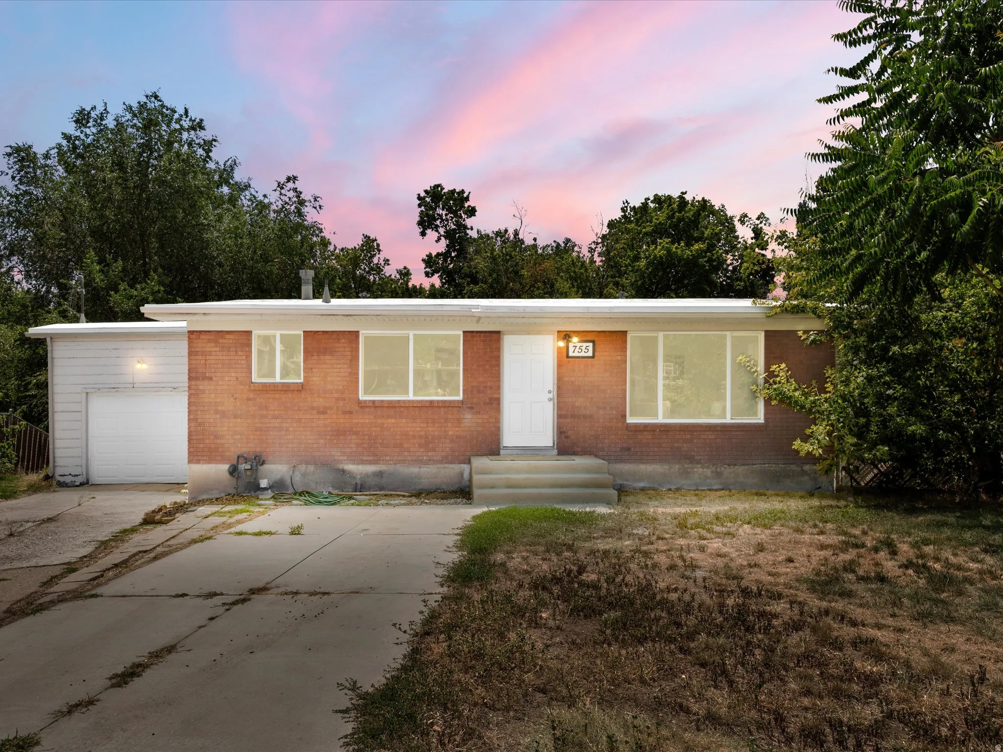 Brick facade residential structure featuring a white entry door, multiple windows, and an attached garage with a white door