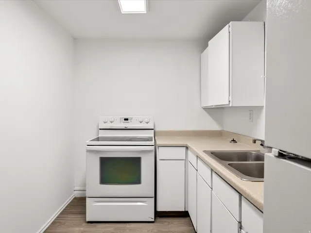 Compact kitchen featuring white cabinetry, a double basin stainless steel sink, light-toned countertops, a white electric range, and wood-finish flooring
