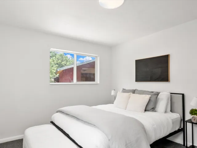 Bright bedroom featuring a double-pane window, flush-mount ceiling light, light gray painted walls, and dark gray carpet flooring