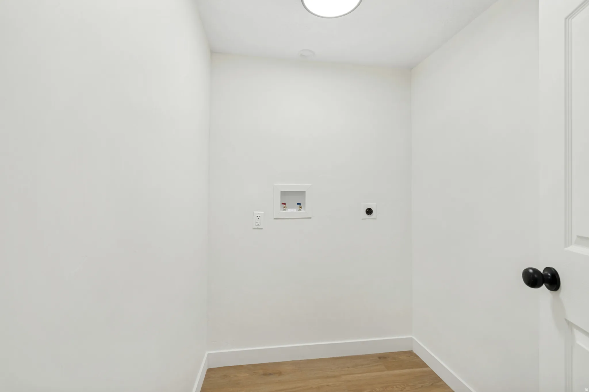Dedicated utility space featuring light wood-finish flooring, white walls, and a round overhead light fixture