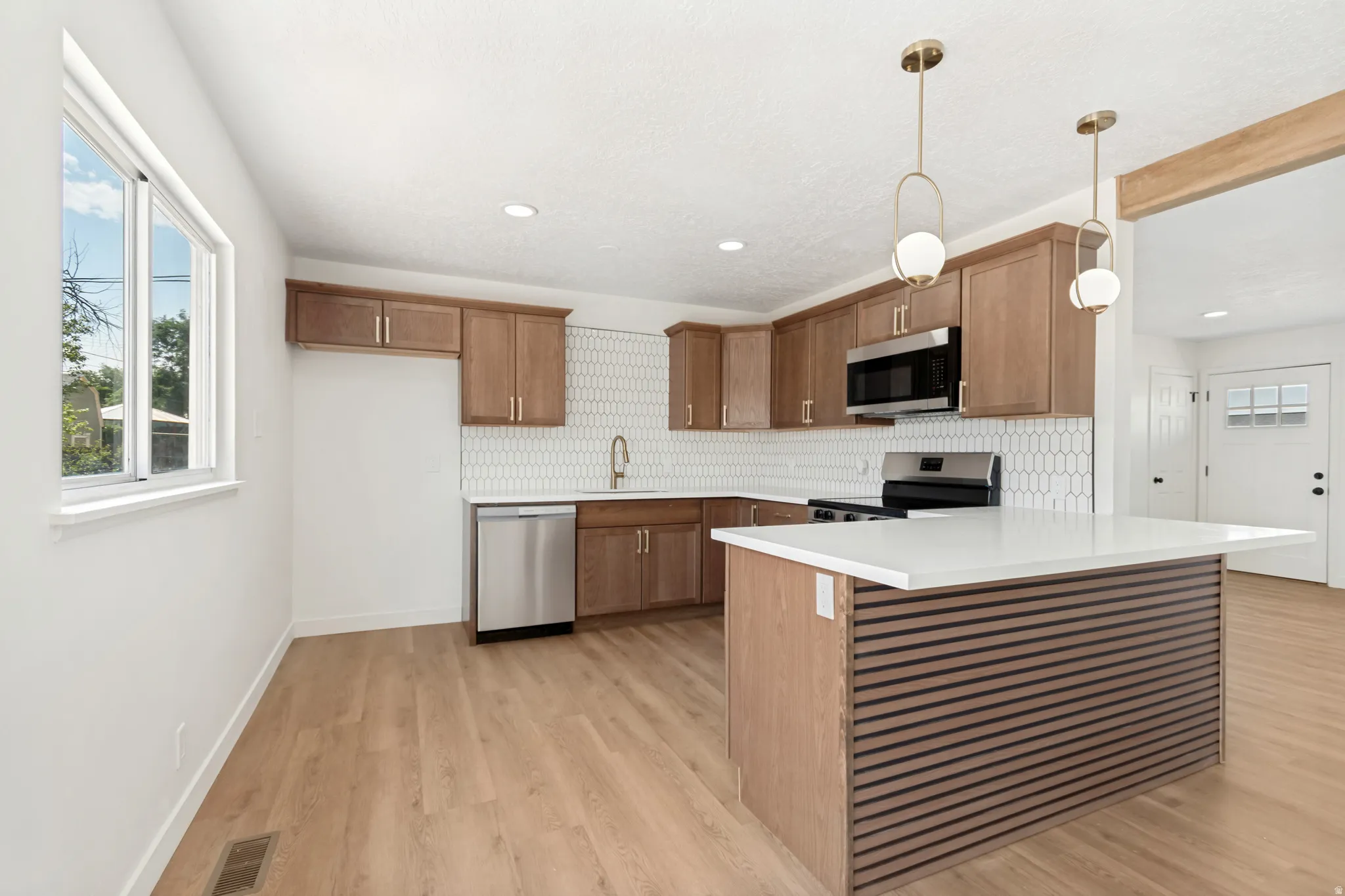 Kitchen featuring wood-finish cabinetry, stainless steel appliances, a hexagon tile backsplash, and an island with a white countertop and slatted wood-finish paneling