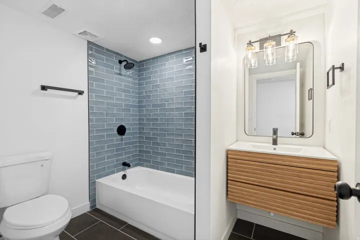 Bathroom featuring a floating wood-finish vanity with an integrated sink, matte black fixtures, and a subway-tiled shower/tub combination