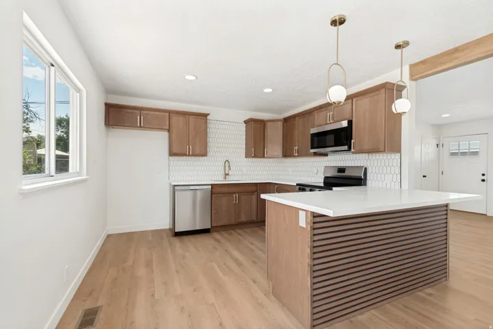 Kitchen featuring wood-finish cabinetry, stainless steel appliances, a hexagon tile backsplash, and an island with a white countertop and slatted wood-finish paneling