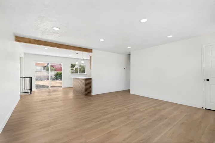 Open-concept living area featuring wood-finish flooring, recessed lighting, and a prominent wood beam accent