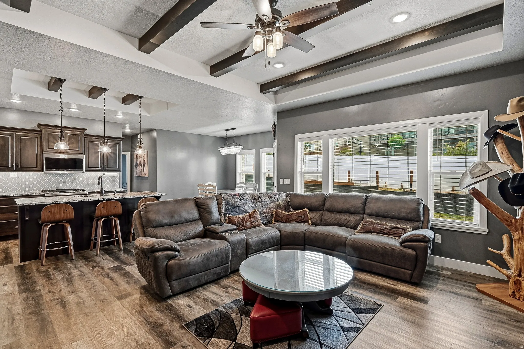 Spacious open-concept living area featuring wood-finish flooring, exposed ceiling beams, and recessed lighting