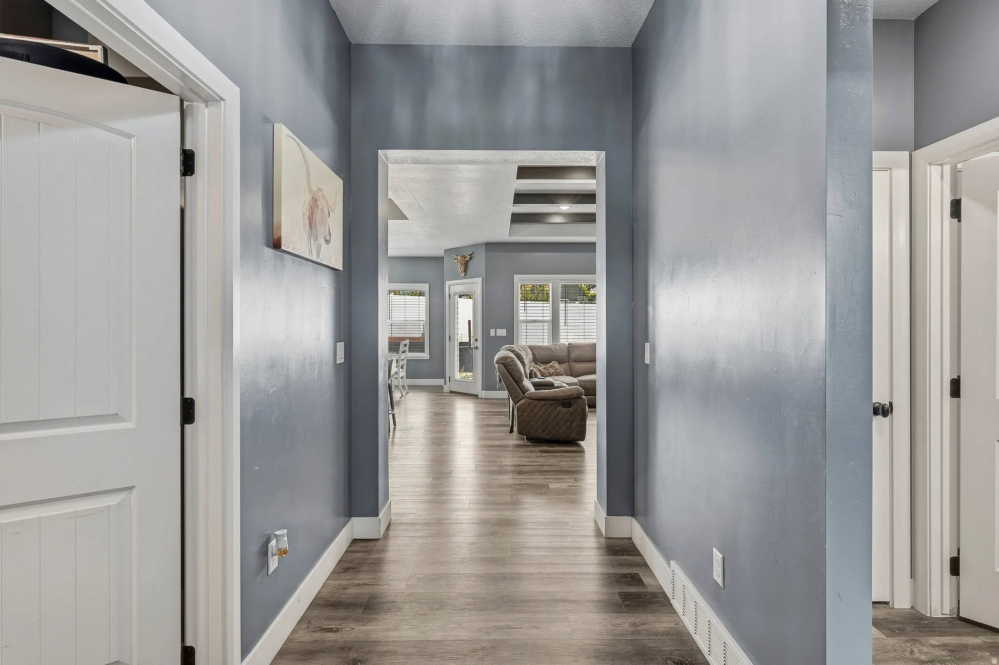 Hallway featuring wood-finish flooring, white trim, and a wide entryway leading to an open living area