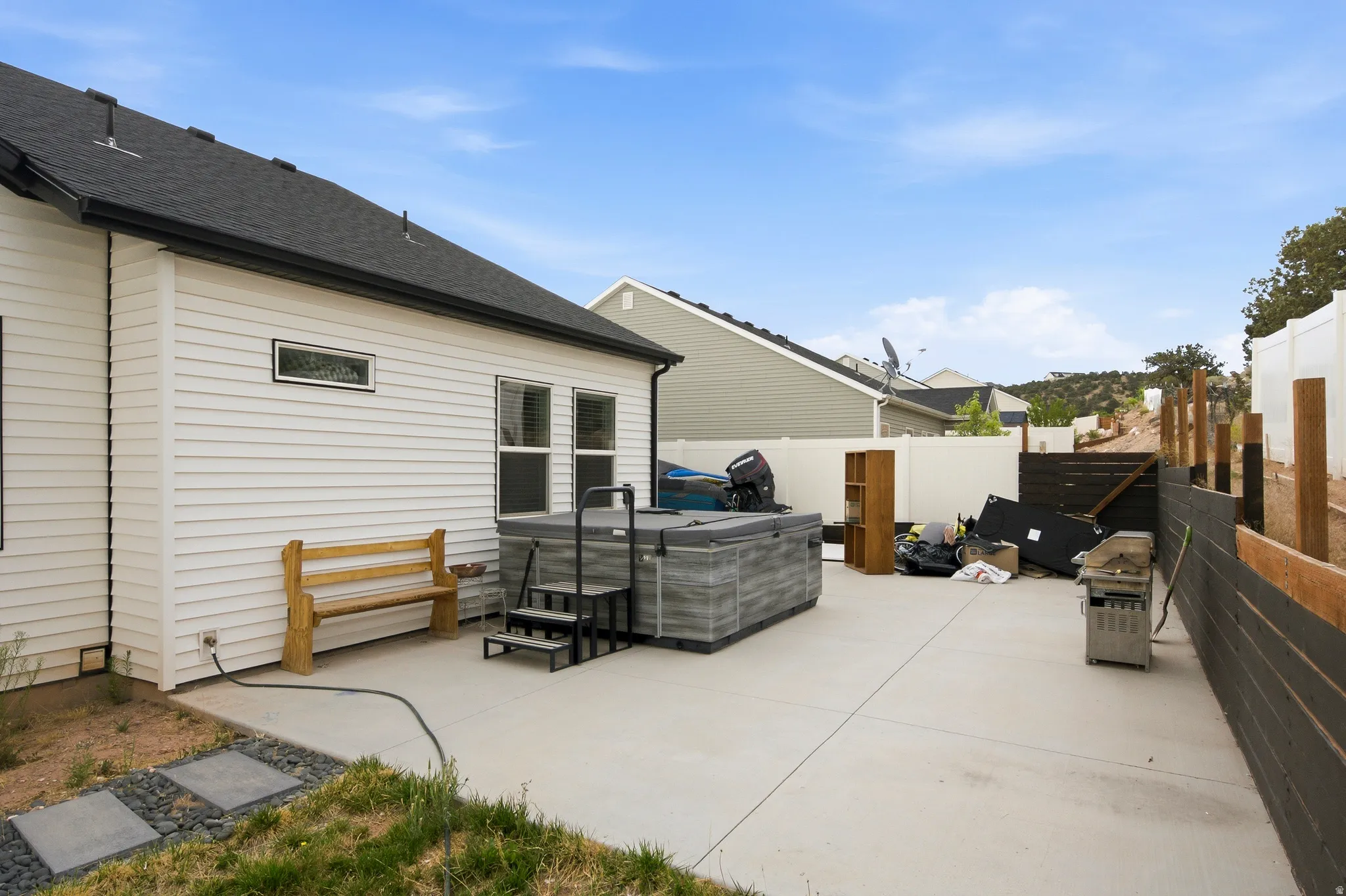 Patio area featuring a hot tub, concrete paving, white siding, and a black shingle roof