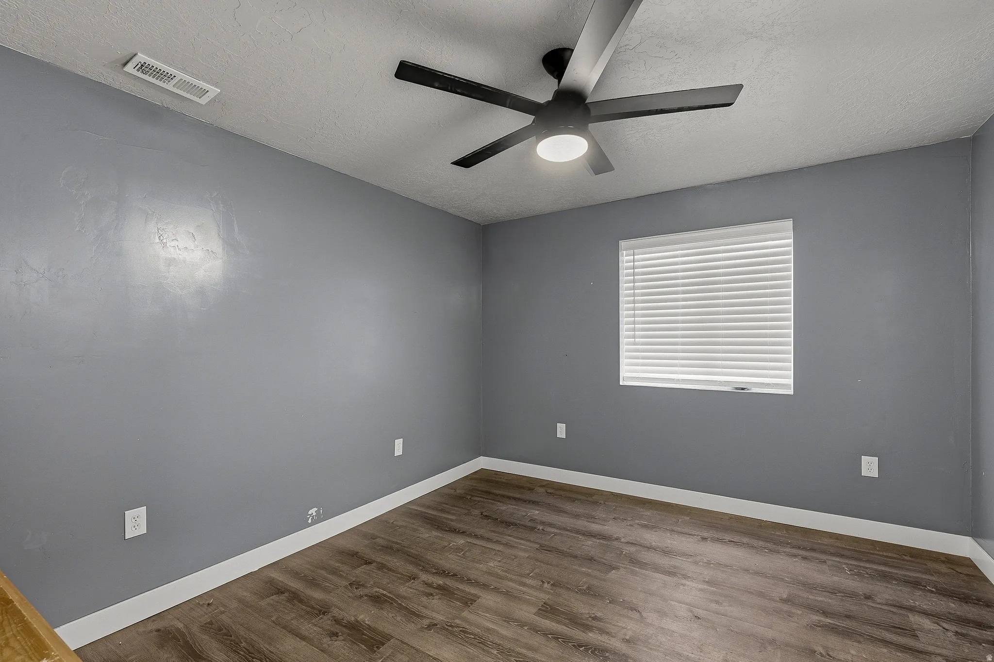 Room featuring wood-finish flooring, a ceiling fan with integrated lighting, a window with horizontal blinds, and grey painted walls with white trim