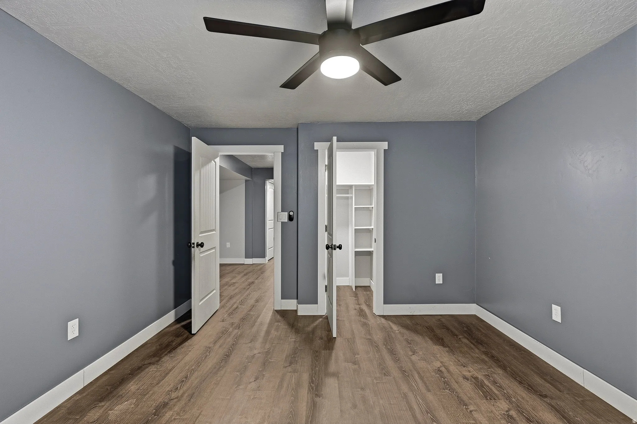 Room featuring wood-finish flooring, a modern ceiling fan with integrated lighting, and a closet with built-in shelving