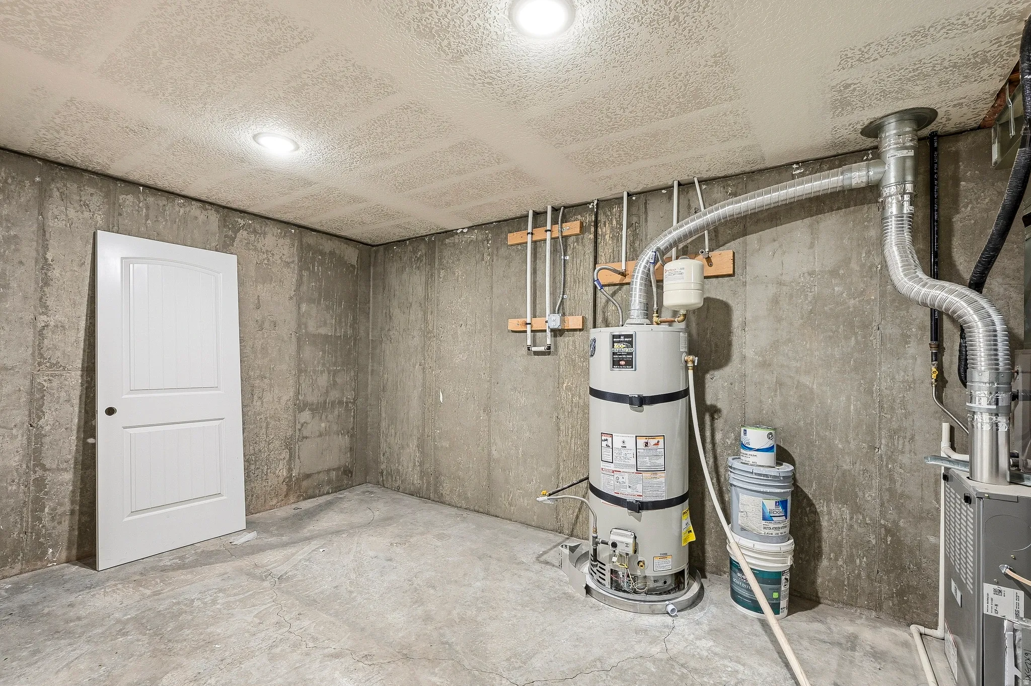 Unfinished basement space featuring concrete walls, a concrete floor, and exposed utilities including a water heater and ventilation ductwork