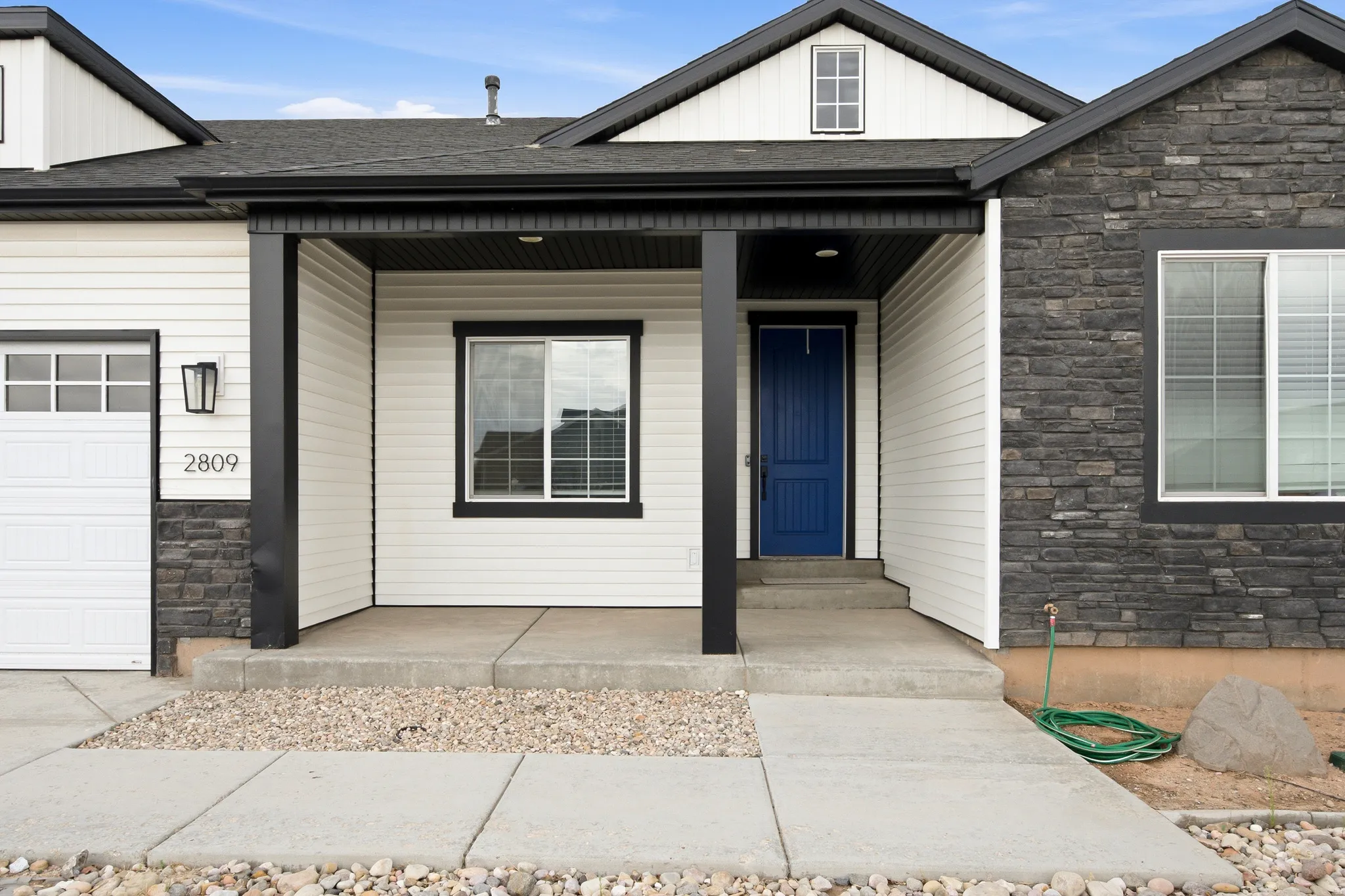 Modern residence featuring contrasting stone and siding facade, a prominent blue entry door, and a covered porch