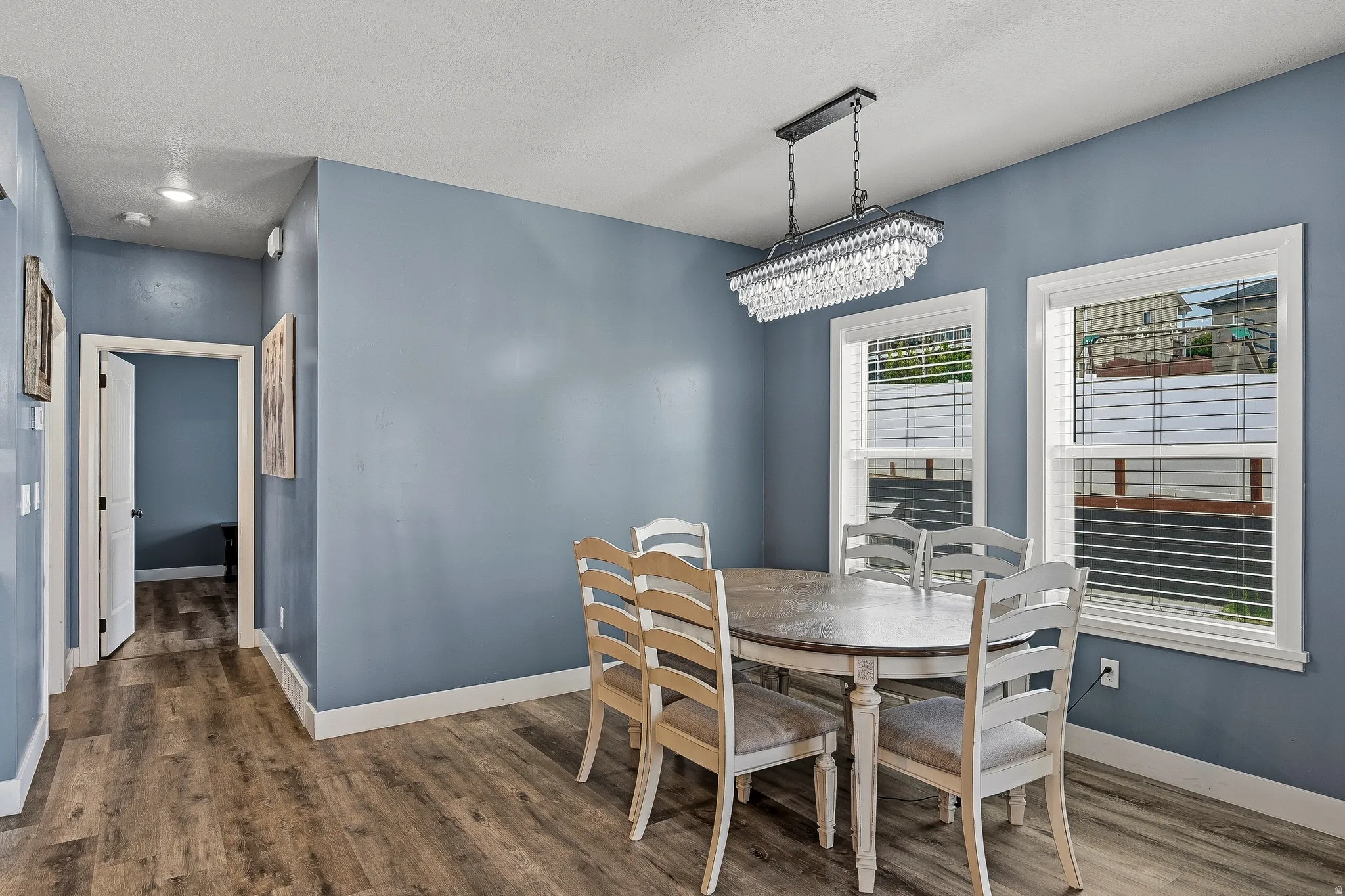 Dining area with wood-finish flooring, two large windows, and a linear crystal chandelier