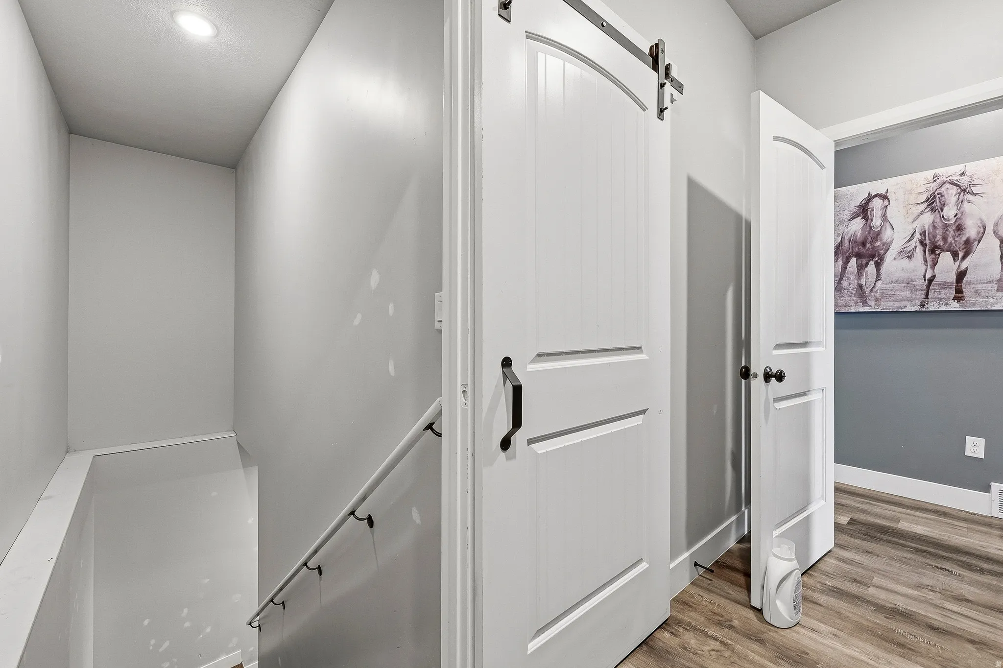 Hallway featuring wood-finish flooring, a barn door with black hardware, white trim, and a recessed ceiling light