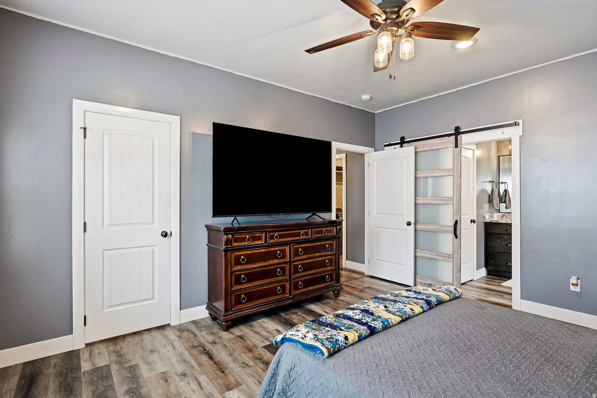Bedroom featuring wood-finish flooring, a ceiling fan with integrated lighting, and a barn door entry to an additional space