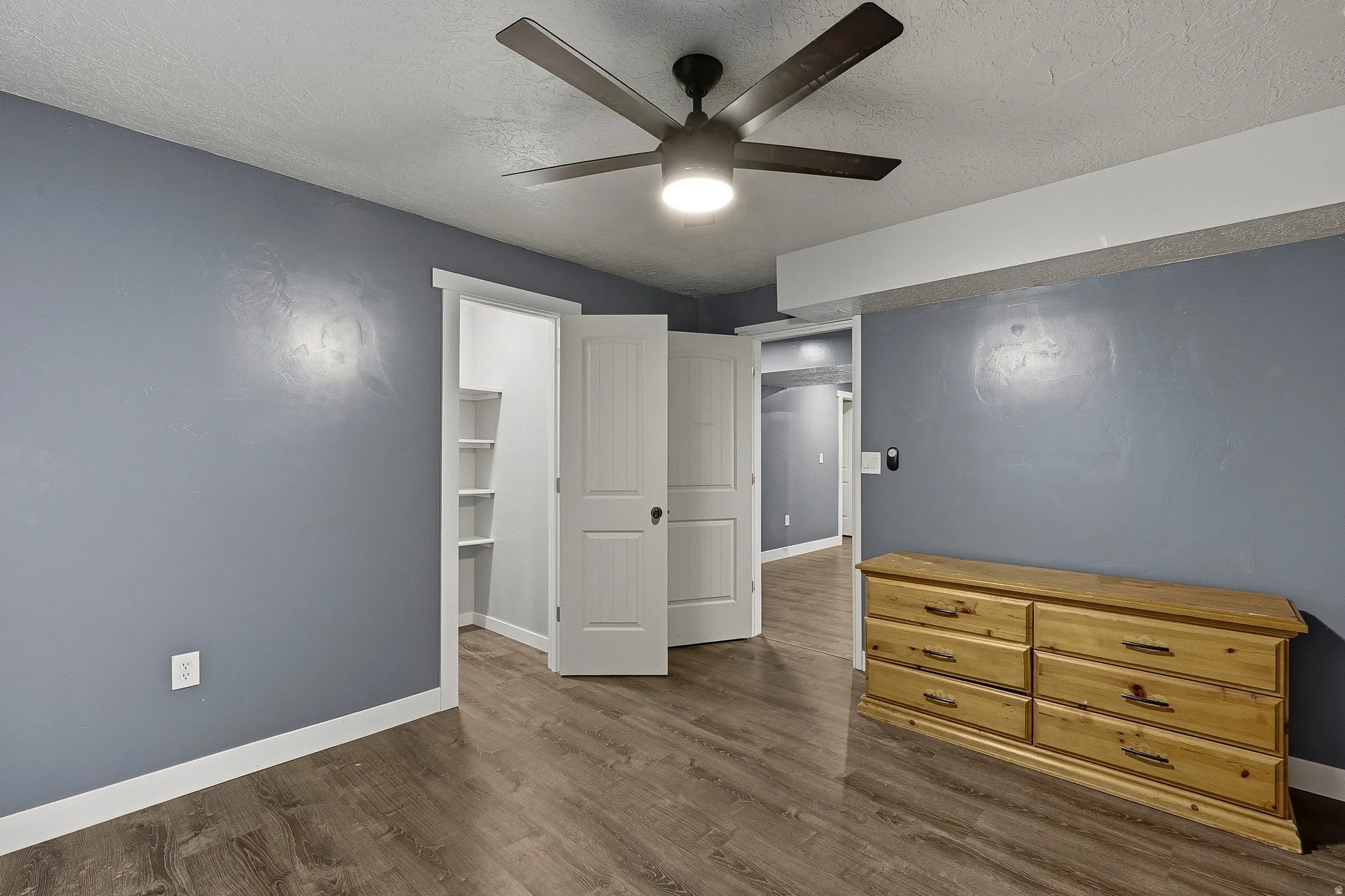 Room featuring wood-finish flooring, a ceiling fan with integrated lighting, and multiple white paneled doors