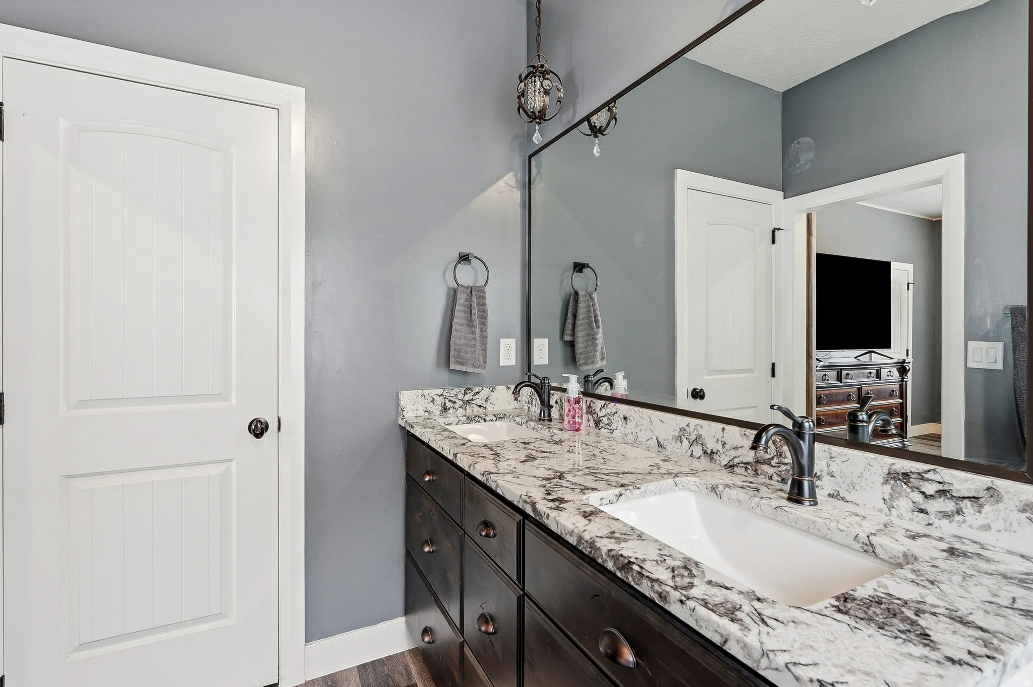 Dual basin vanity featuring a patterned natural stone countertop, undermount sinks, dark wood-finish cabinetry with bronze hardware, and matte black faucets