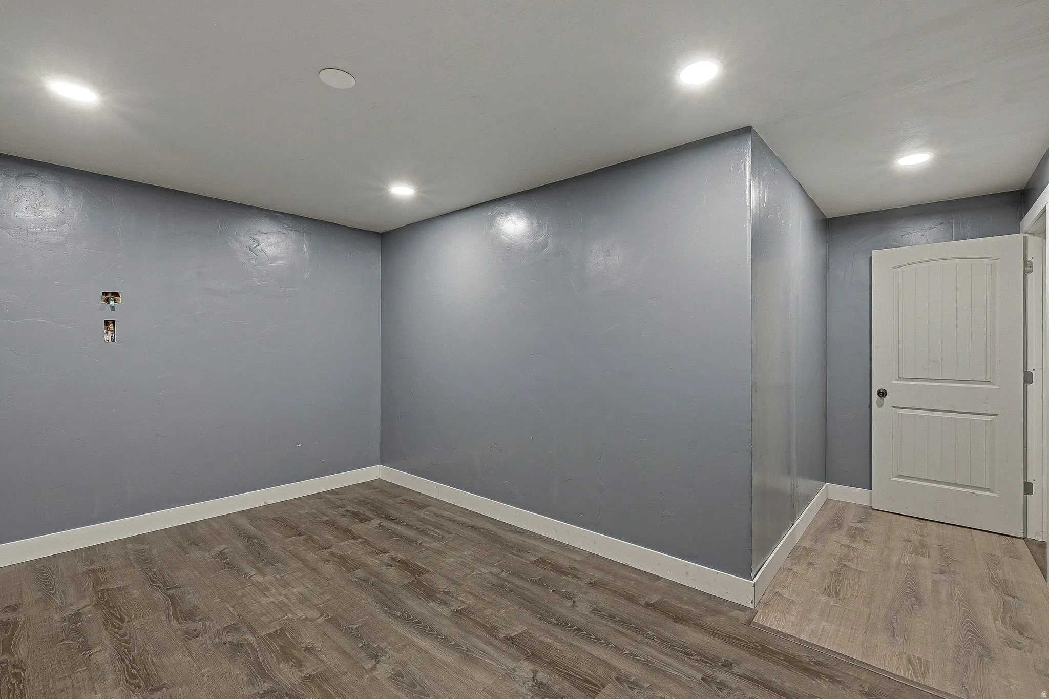 Room featuring wood-finish flooring, recessed lighting, and a white interior door
