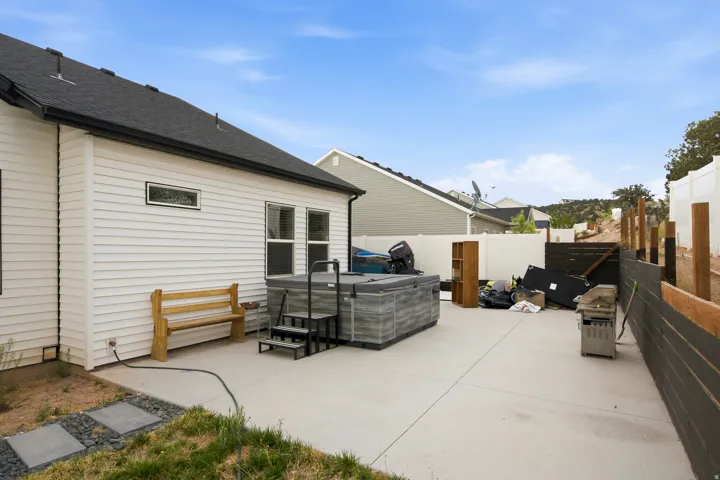Patio area featuring a hot tub, concrete paving, white siding, and a black shingle roof