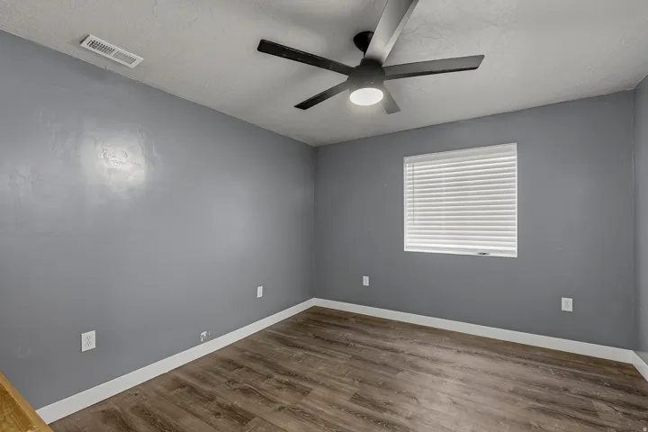 Room featuring wood-finish flooring, a ceiling fan with integrated lighting, a window with horizontal blinds, and grey painted walls with white trim