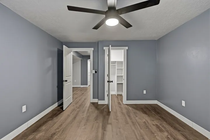Room featuring wood-finish flooring, a modern ceiling fan with integrated lighting, and a closet with built-in shelving