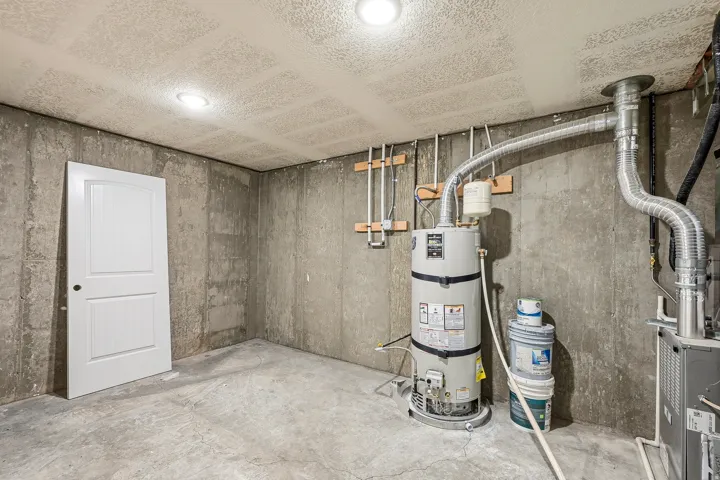 Unfinished basement space featuring concrete walls, a concrete floor, and exposed utilities including a water heater and ventilation ductwork