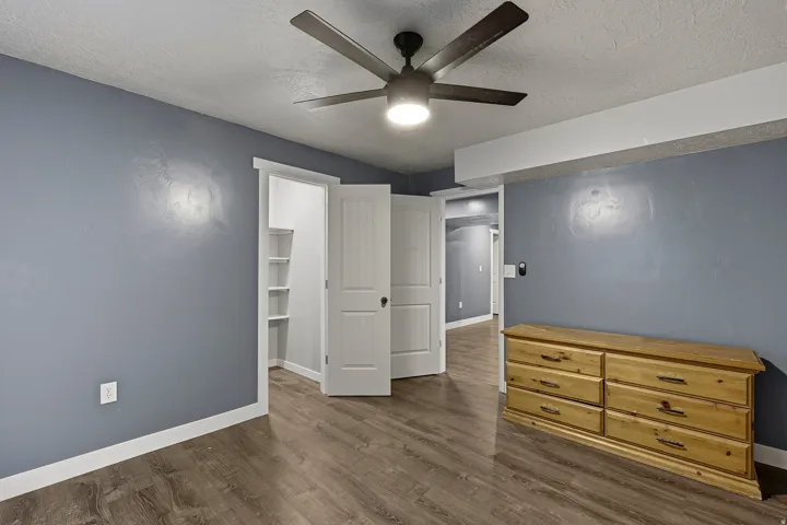 Room featuring wood-finish flooring, a ceiling fan with integrated lighting, and multiple white paneled doors