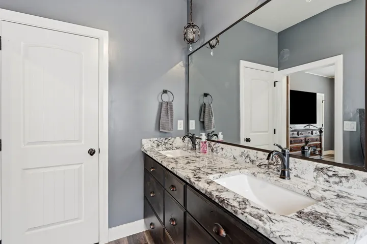 Dual basin vanity featuring a patterned natural stone countertop, undermount sinks, dark wood-finish cabinetry with bronze hardware, and matte black faucets