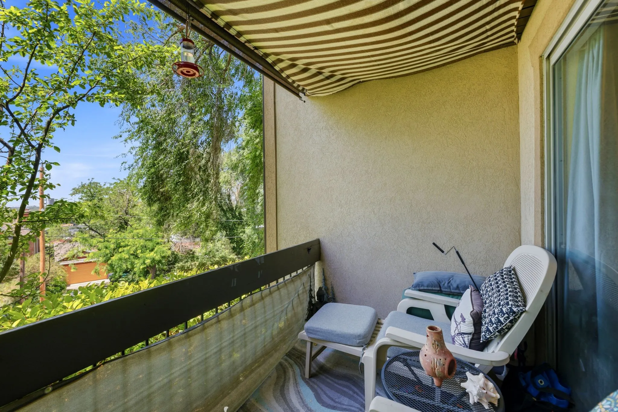 Private balcony featuring a striped awning, stucco exterior, and a sliding glass door