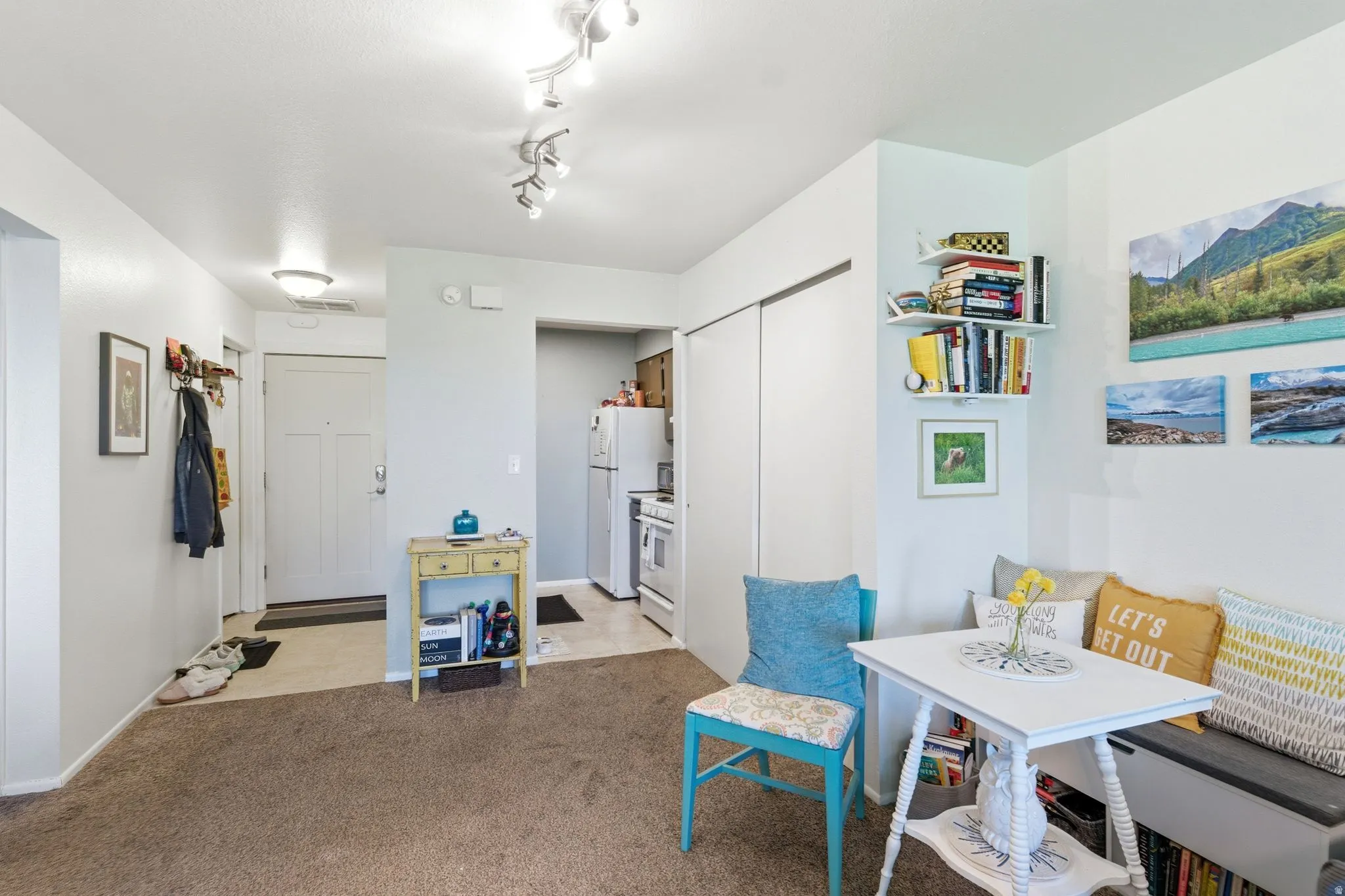 Interior living space featuring track lighting, a dedicated entry area with a paneled door, and a kitchen alcove with white appliances