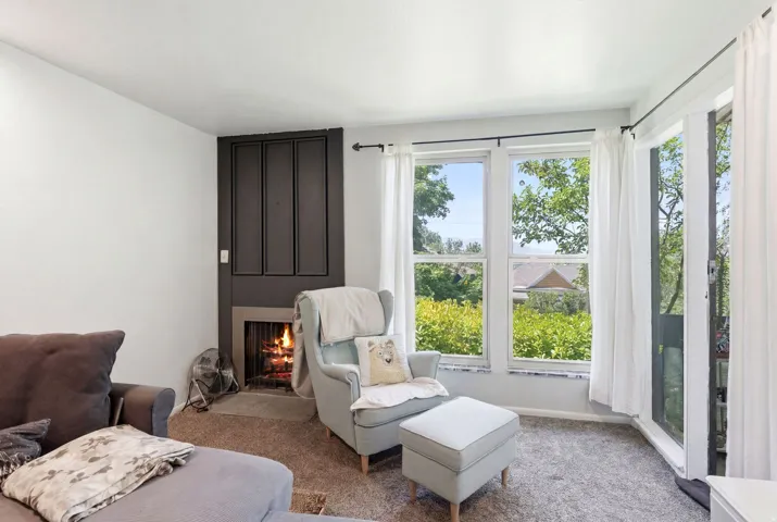 Living area with a dark paneled fireplace surround, multiple windows, and a glass door