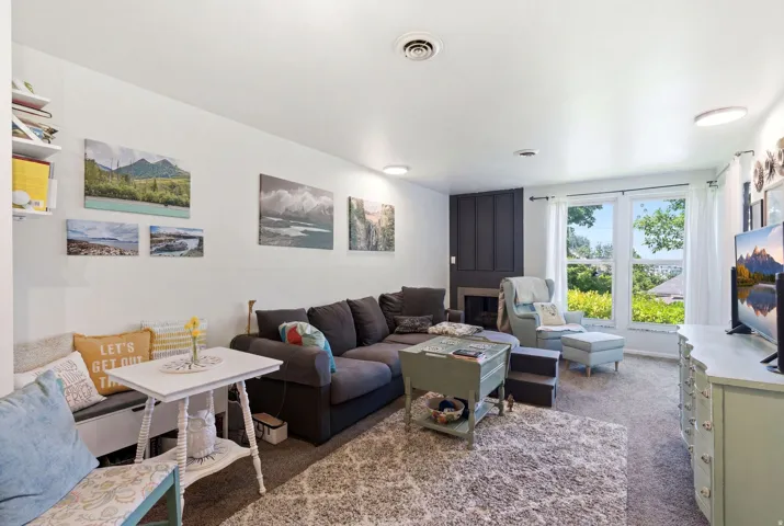 Living room featuring a dark paneled fireplace surround, carpet flooring, and a large window with white trim