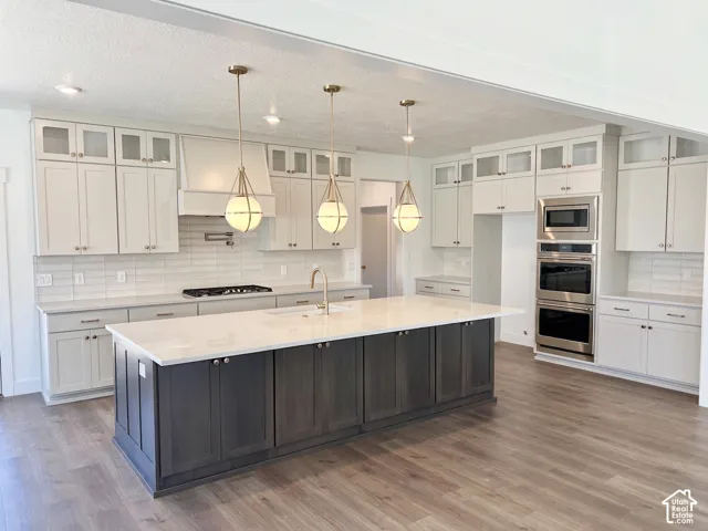 Gourmet kitchen featuring a large two-tone island with a light-toned countertop, stainless steel appliances, a gas range with a pot filler, and white shaker cabinetry with glass-front upper cabinets