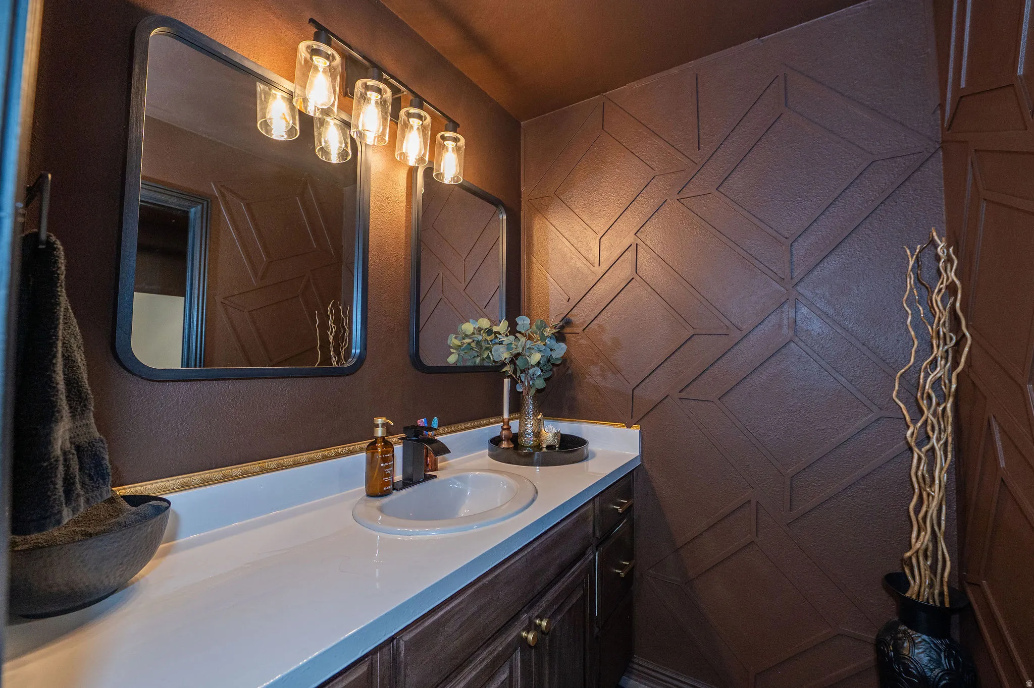 Bathroom vanity featuring a single basin sink, white countertop, and dark wood-finish cabinetry with brass hardware