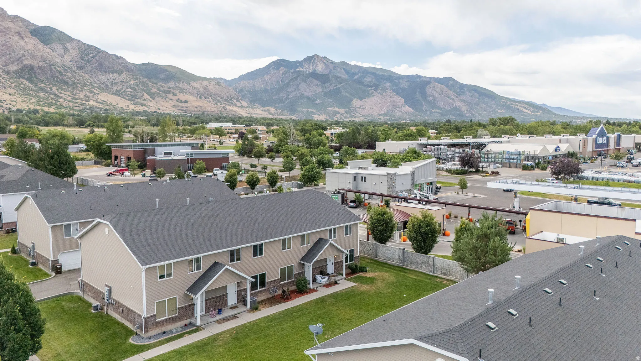 Townhome complex with mountain backdrop, featuring light-colored siding, dark shingle roofs, and green lawn areas