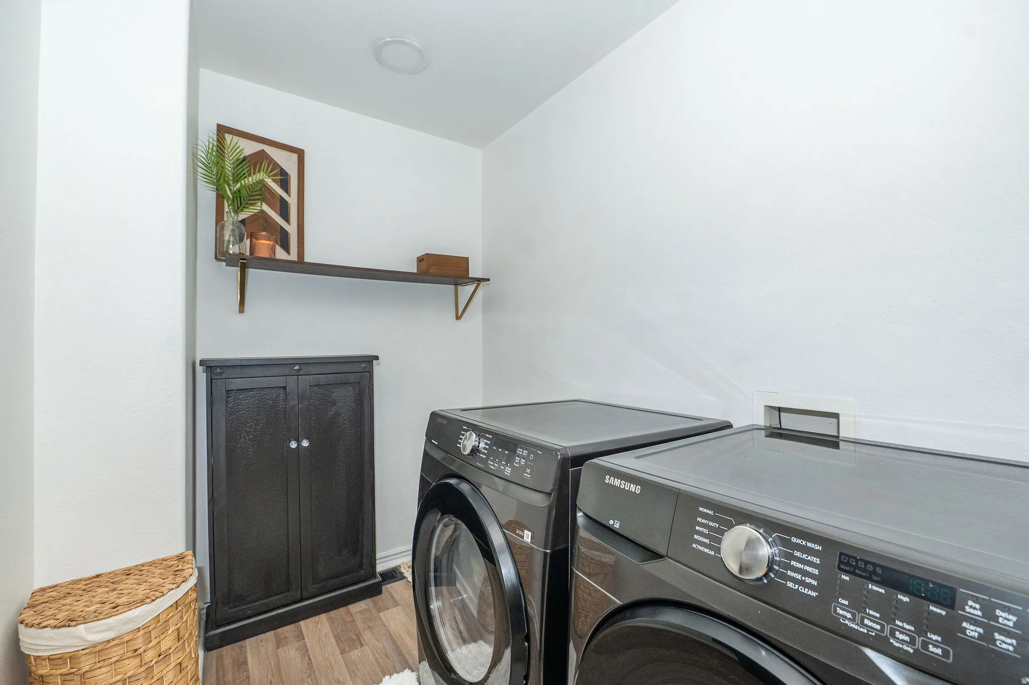 Dedicated laundry space featuring wood-finish flooring and a built-in dark wood storage cabinet