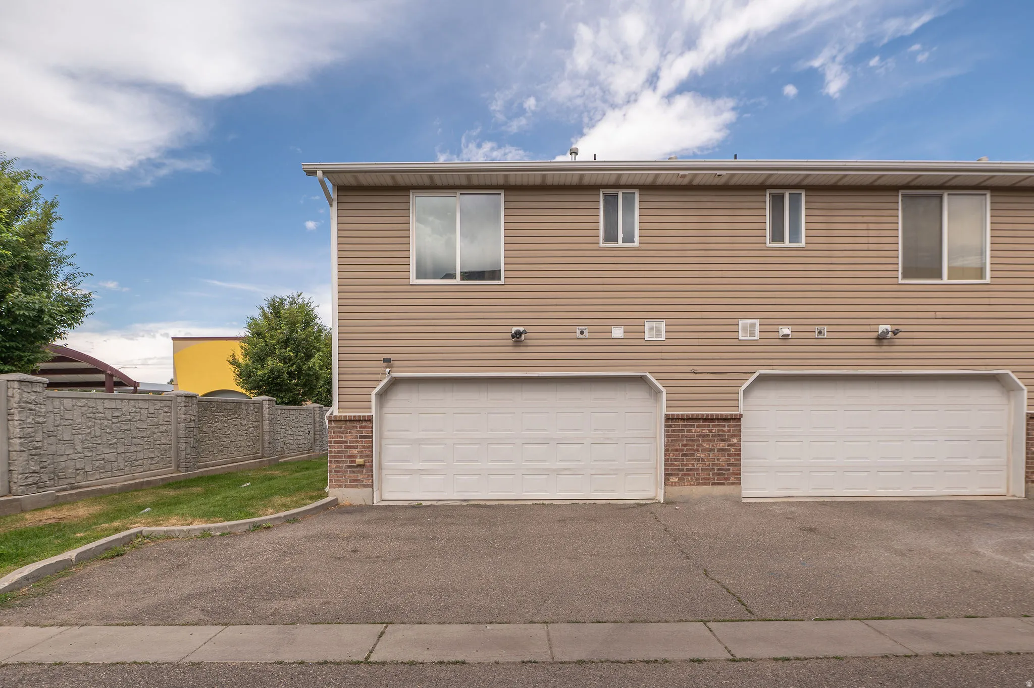 Exterior facade featuring tan horizontal siding, brick accents, white frame windows, and two white garage doors