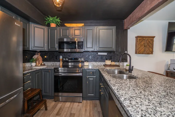 Contemporary kitchen featuring dark cabinetry, granite countertops, and stainless steel appliances