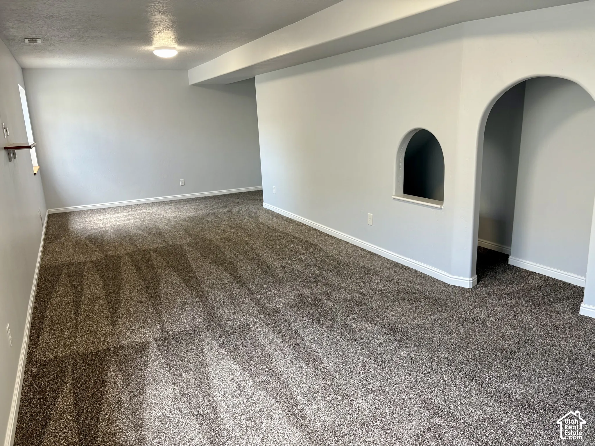 Spacious room featuring neutral-toned walls, recessed lighting, and a textured carpeted floor
