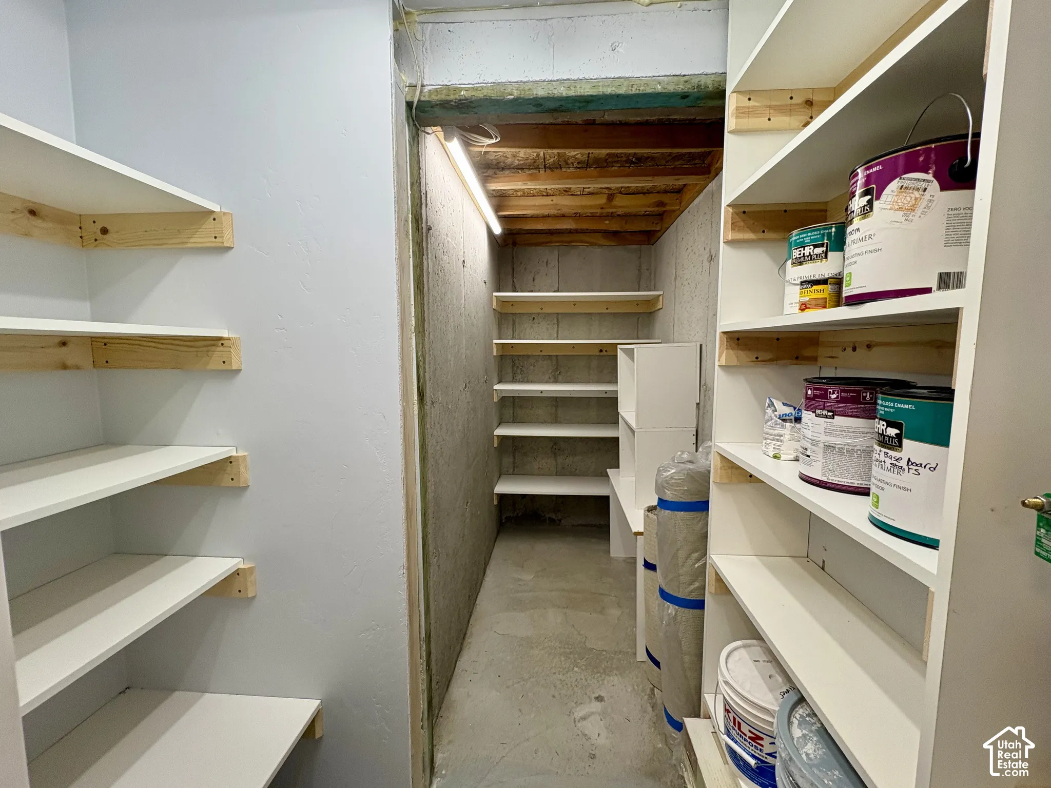 Dedicated storage area featuring extensive built-in shelving, concrete flooring, and overhead lighting