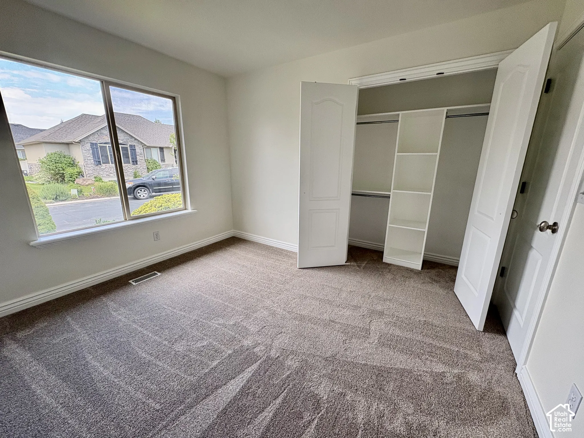 Bright room featuring a large window, neutral carpeting, and a built-in closet with shelving and hanging rods