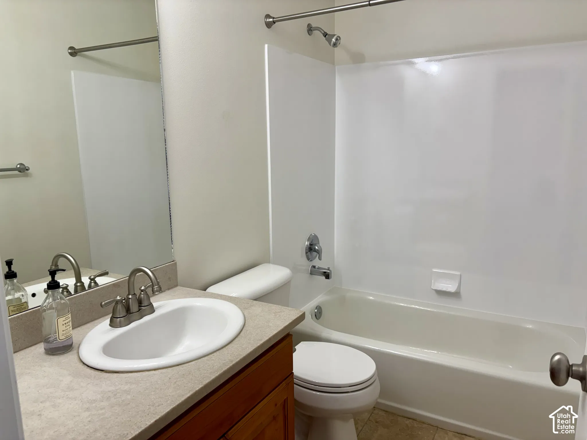 Bathroom featuring a white bathtub and shower surround, a vanity with an integrated sink, a light-toned countertop, and wood-finish cabinetry