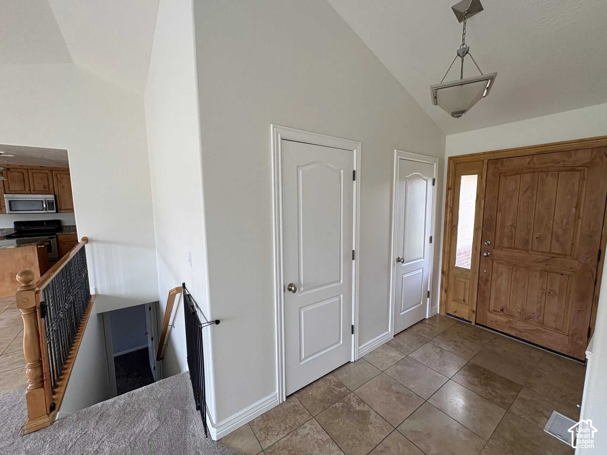 Entryway featuring a wood-panel door with a sidelight, neutral tile flooring, and a vaulted ceiling