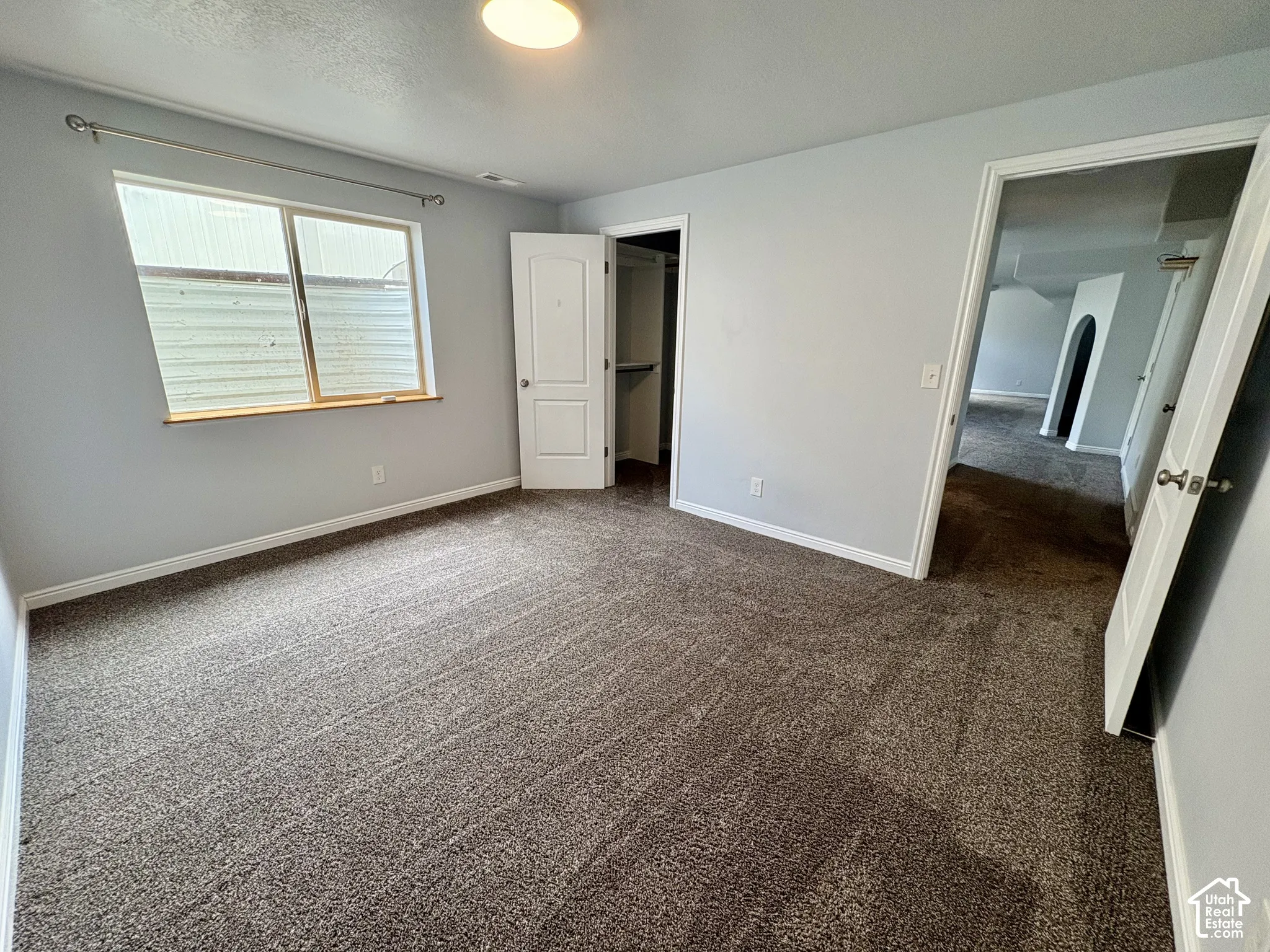 Carpeted room with light gray walls, a window with wood trim, a built-in closet with bifold doors, and a ceiling-mounted light fixture