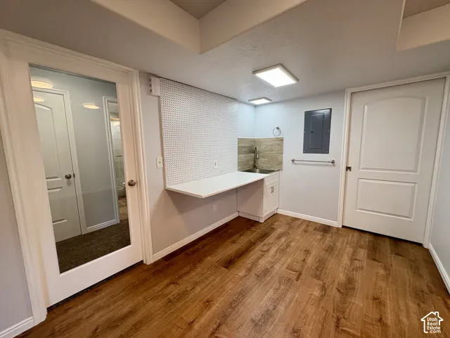 Utility area featuring wood-finish flooring, a white floating desk with pegboard, a stainless steel sink with tiled backsplash, and recessed lighting